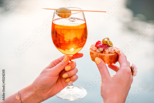 Female hand holding glass with Spritz Aperol alcohol drink decorated with olive on the water chanal background in Venice. Image with small depth of field photo