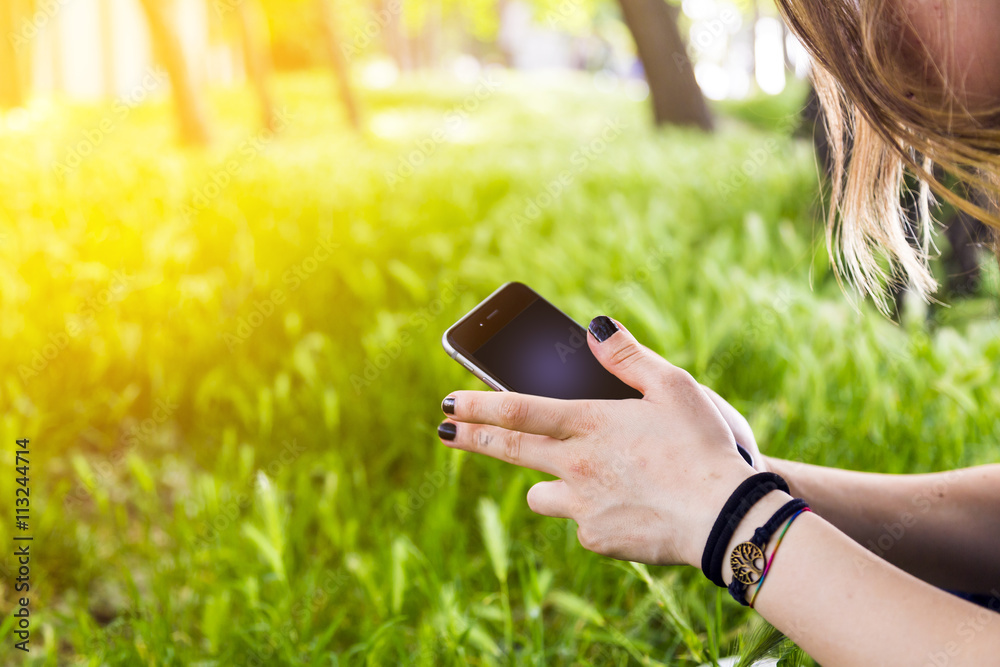 Teenage girl with smartphone outdoors in park. Closeup of female hands and smart phone.