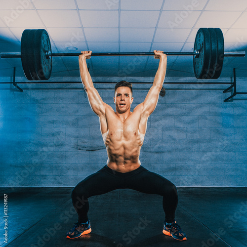 Portrait of a handsome muscular man workout with barbell in fitness gym