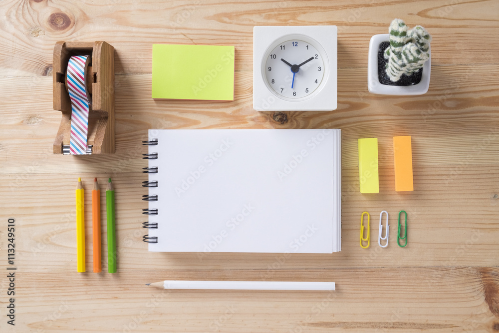 Topview of office stuff on wooden working table. Mock up. Sticky tape, note paper , white blank notebook, post-it note, pencil, clock, paper clip, colour pencil and cattus. Topview of office stuff on wooden working table. Mock up. Sticky tape, note paper , white blank notebook, post-it note, pencil, clock, paper clip, colour pencil and cattus.