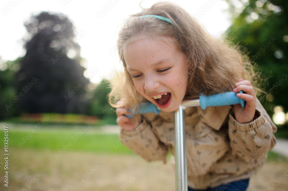 Lttle girl cheerfully laughs having leaned against a wheel of the scooter.