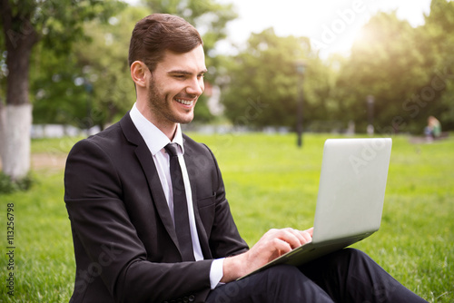 Handsome delighted man sitting on the grass