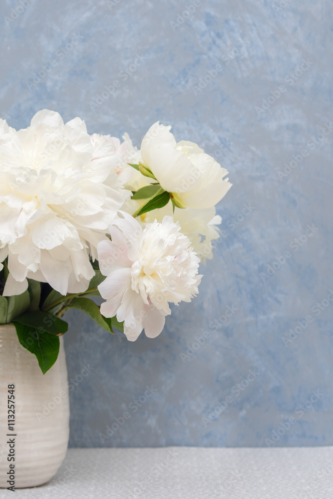 Bouquet of white peonies in ceramic vase against gray-blue venetian stucco wall. Selective focus on the flowers. Bouquet of white peonies in ceramic vase against gray-blue venetian stucco wall. Selective focus on the flowers.