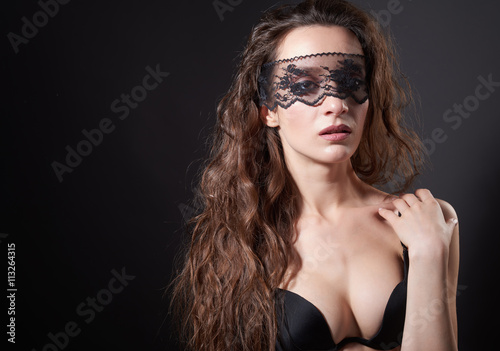 Sensual woman posing over dark background with lace mask on eyes
