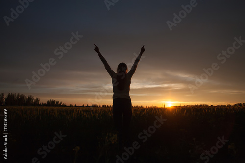 woman with open arms in the green wheat field at the morning.