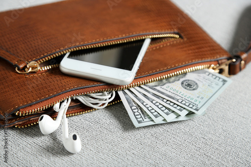 Leather purse with mobile phone and dollar banknotes on grey cloth background