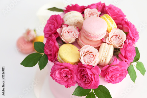 Tasty macaroons and roses in box on light background