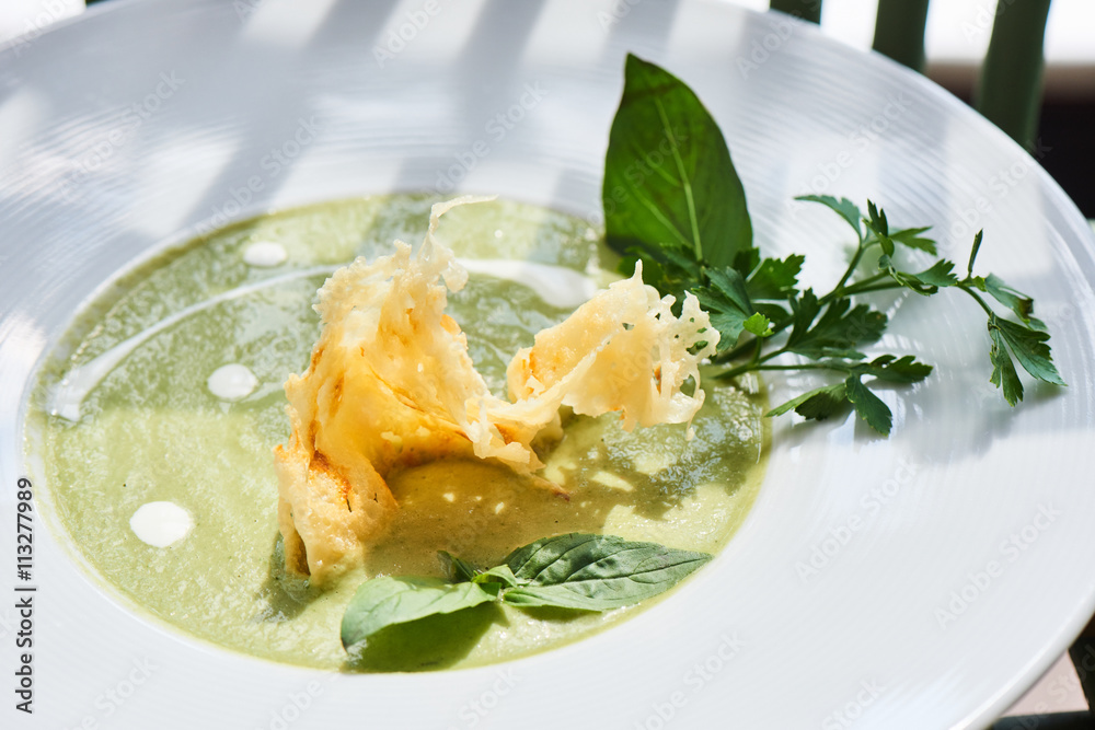 Soup puree zucchini, chicken broth and Parmesan crisp in a white plate Soup puree zucchini, chicken broth and Parmesan crisp in a white plate