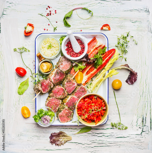 Meat skewers with fresh cutting vegetables and seasoning on enamel  plate . Meat skewers  for grill or cooking, preparation on light rustic background, top view