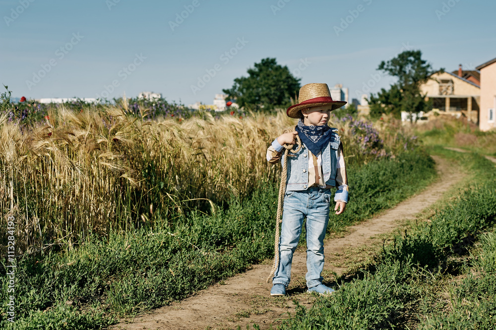 Fototapeta premium Little boy dressed in Western style in the field , retro style