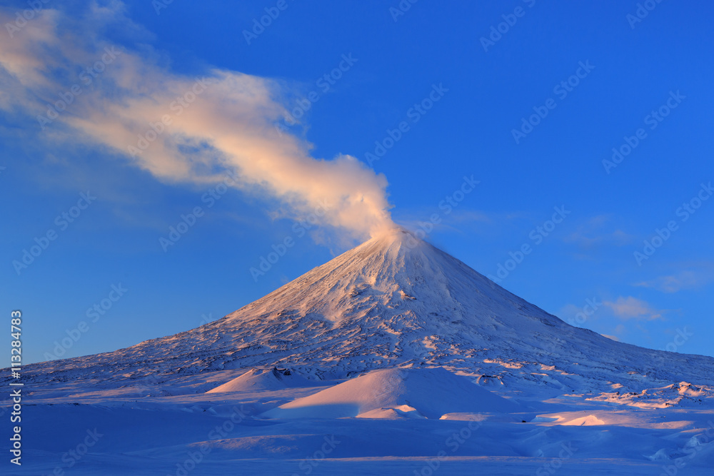 Winter volcanic landscape of Kamchatka Peninsula: view of erupting active Klyuchevskaya Sopka at sunrise. Eurasia, Russian Far East, Kamchatka Region, Klyuchevskaya Group of Volcanoes.