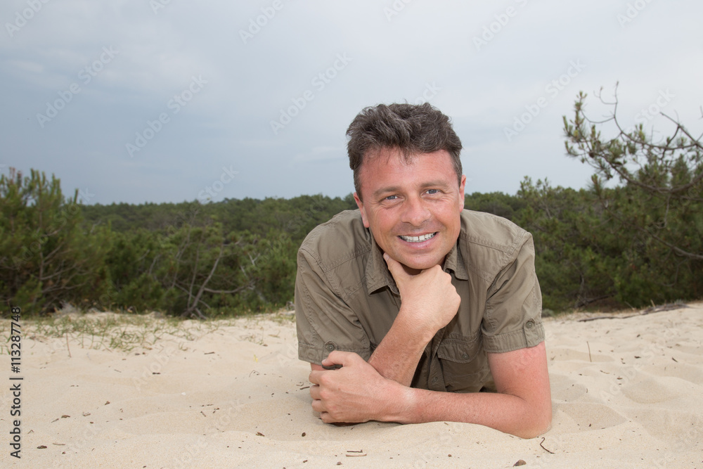 Man on beach lying in sand looking to side smiling Man on beach lying in sand looking to side smiling