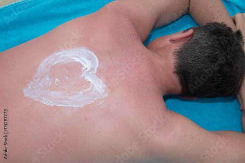 Man with suntan lotion at the beach in form of the heart
