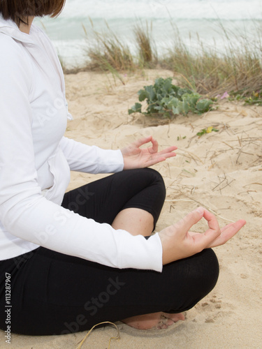 Woman meditating on the beach sitting on summer