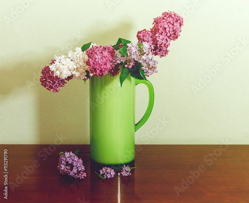 Two Branch of White and Purple Lilac in the Green Plastic Pitcher.Wooden Table photo