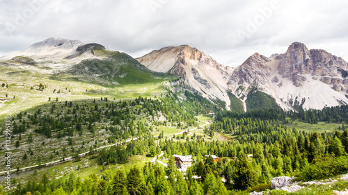 Panoramic view to alpine huts in green valleys surrounded by the mountains and snow picks, a trekking route Alta Via 1, The Dolomites, Alps, South Tyrol, Italy.
