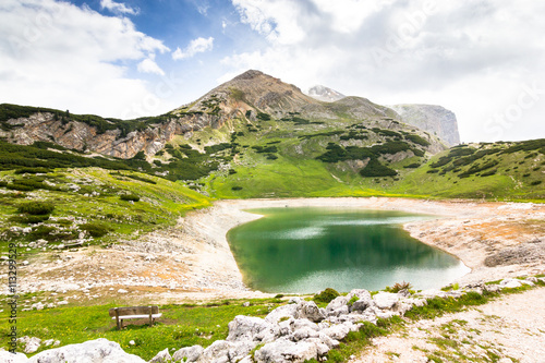 A mountain lake and a bench near by in sunny weather, Alta Via 1 trekking route, The Dolomites, Alps, South Tyrol, Italy.