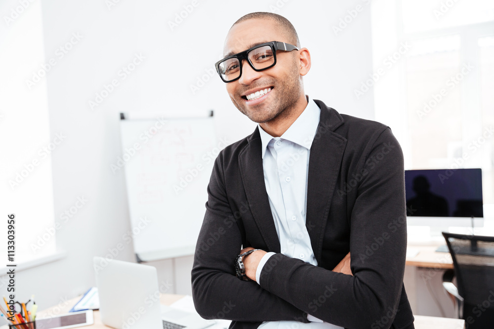 Happy young businessman standing with arms crossed in office Happy young businessman standing with arms crossed in office