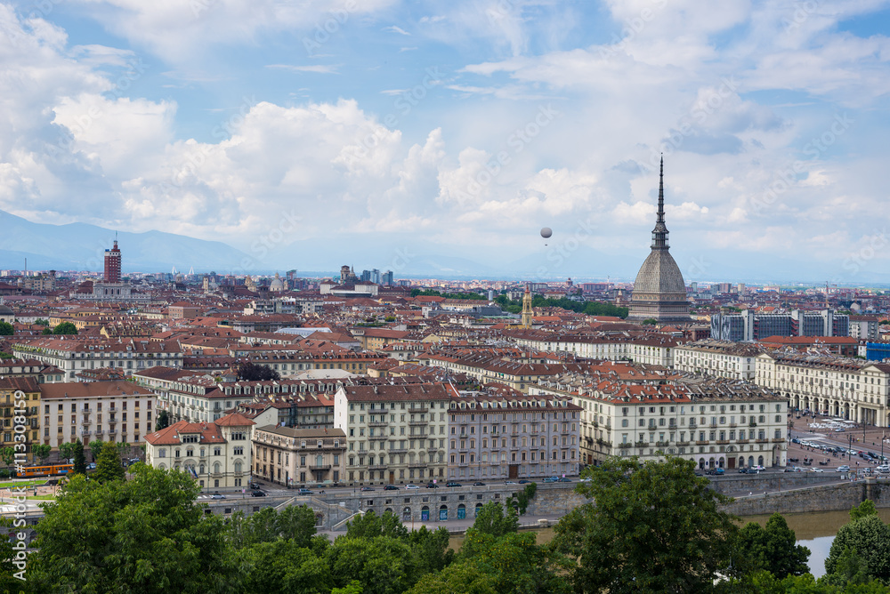 Cityscape of Torino (Turin, Italy) with the Mole Antonelliana and the hot-air baloon towering over the buildings. Wind storm clouds over the Alps in the background.
