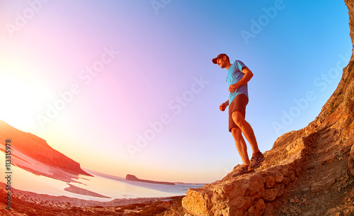 male hiker, traveler runs on the trail against sea and blue sky at the sunset. Balos beach on background, Crete, Greece