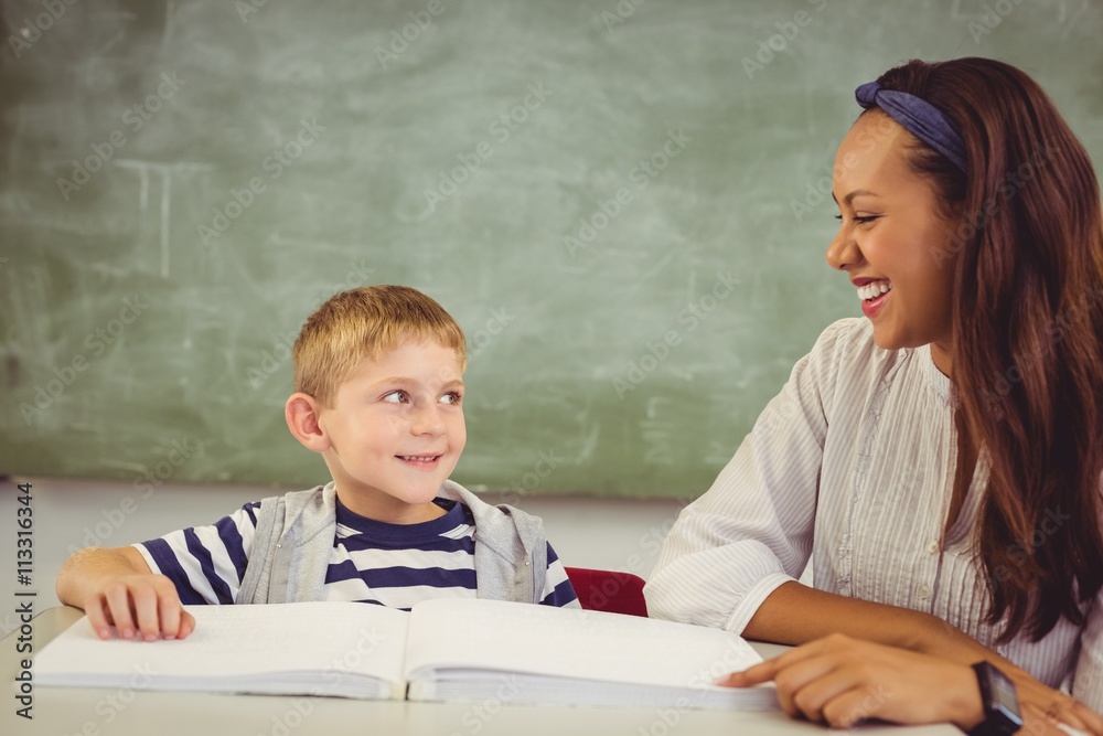Teacher helping a boy with his homework in classroom Teacher helping a boy with his homework in classroom