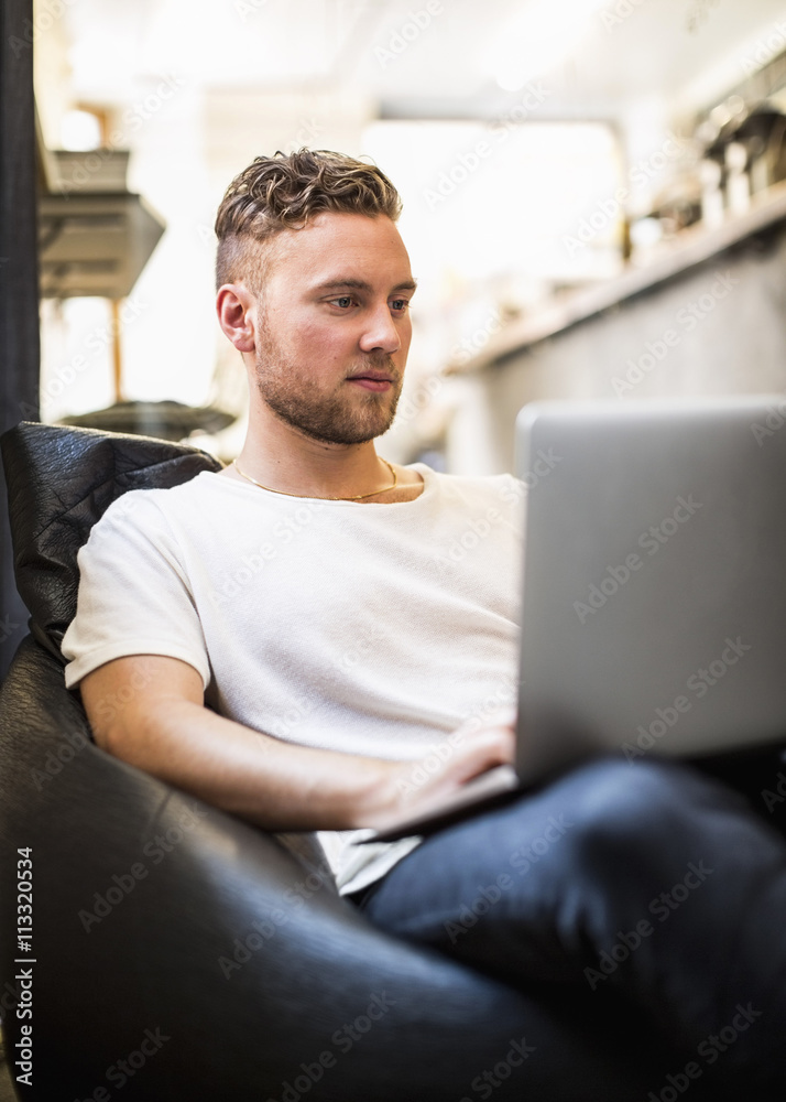 Young businessman using laptop while sitting on bean bag in new office Young businessman using laptop while sitting on bean bag in new office