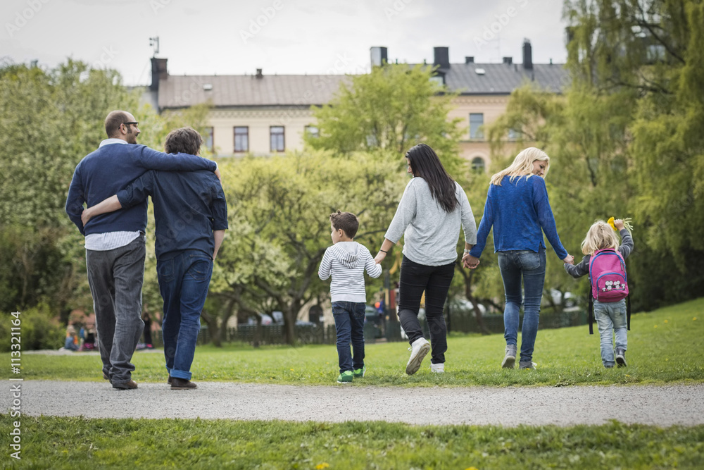 Rear view of female homosexual family walking at park with gay couple in background Rear view of female homosexual family walking at park with gay couple in background