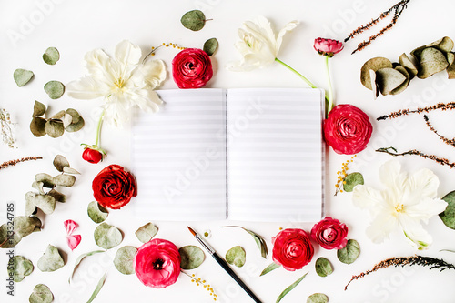 Workspace. Notebook or sketchbook, pink and red roses or ranunculus, white tulips and green leaves on white background. Flat lay, top view
