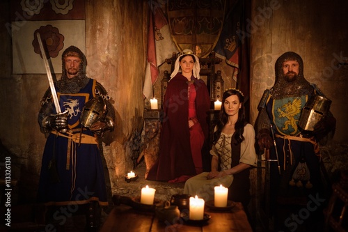 Medieval queen with her courtier and knights on guard in ancient castle interior.