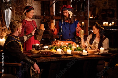 Medieval people eat and drink in ancient castle kitchen interior.