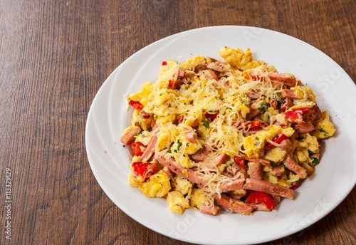 scrambled eggs with ham, vegetables and cheese in a plate on wooden table