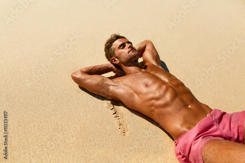 Man Body On Beach In Summer. Handsome Sexy Fit Male With Healthy Skin Sun Tan Tanning At Luxury Relax Spa Resort. Beautiful Fitness Model Relaxing, Sunbathing Lying On Sand. Summertime Travel Vacation