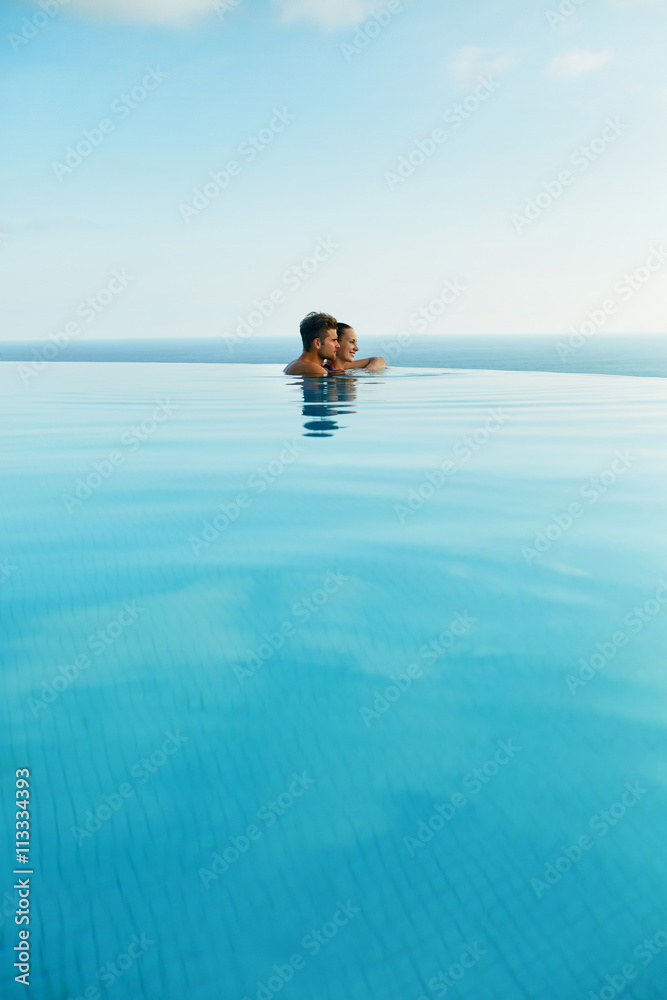 Couple In Love At Luxury Resort On Romantic Summer Vacation. People Relaxing Together In Edge Swimming Pool Water, Enjoying Beautiful Sea View. Happy Lovers On Honeymoon Travel. Relationship, Romance