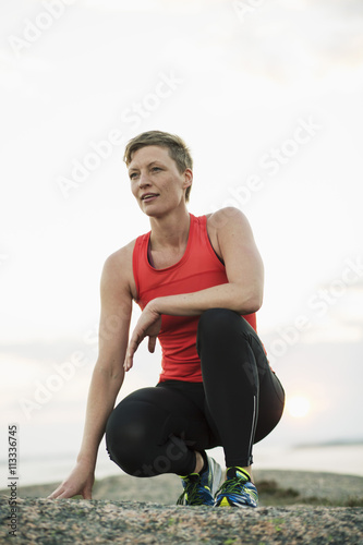 Young woman in sportswear crouching on rock