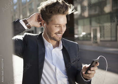 Young businessman smiling while listening music through mobile phone on street photo