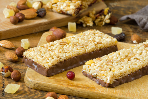 Granola bars with cornflakes, puffed cereals and rolled oats covered in chocolate on wooden cutting board photo