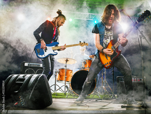 Rock band performs on stage. Guitarist, bass guitar and drums. The guitarist plays solo.