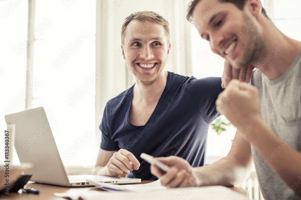 Happy loving homosexual couple with laptop siting at table in home Happy loving homosexual couple with laptop siting at table in home