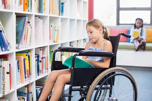 Disabled school girl reading book in library