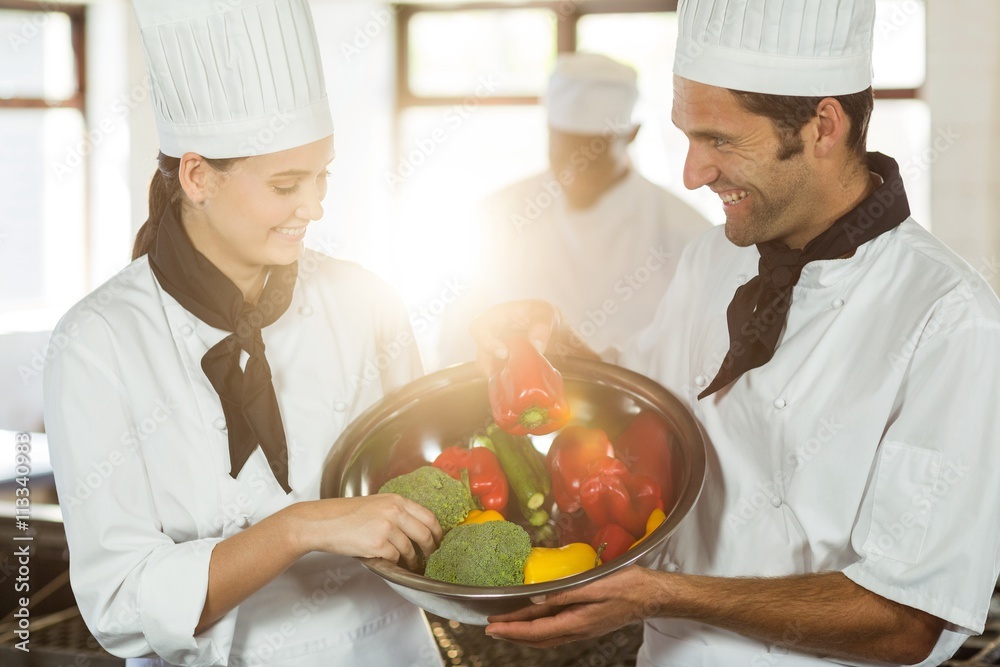 Two smiling chefs holding a bowl of vegetable Two smiling chefs holding a bowl of vegetable