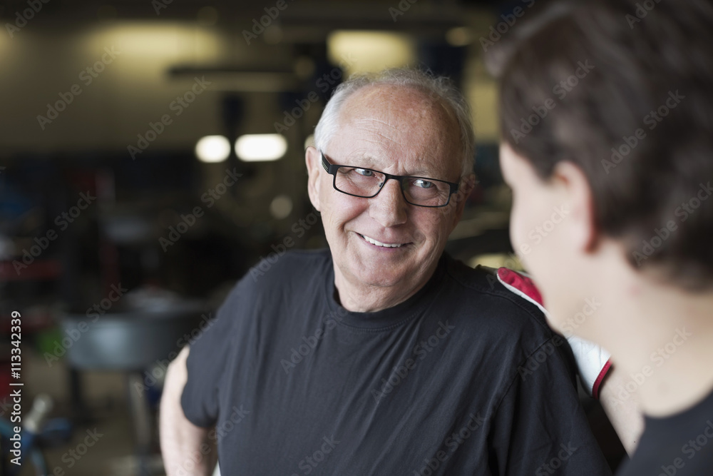 Happy senior male mechanic smiling at coworker in auto repair shop Happy senior male mechanic smiling at coworker in auto repair shop