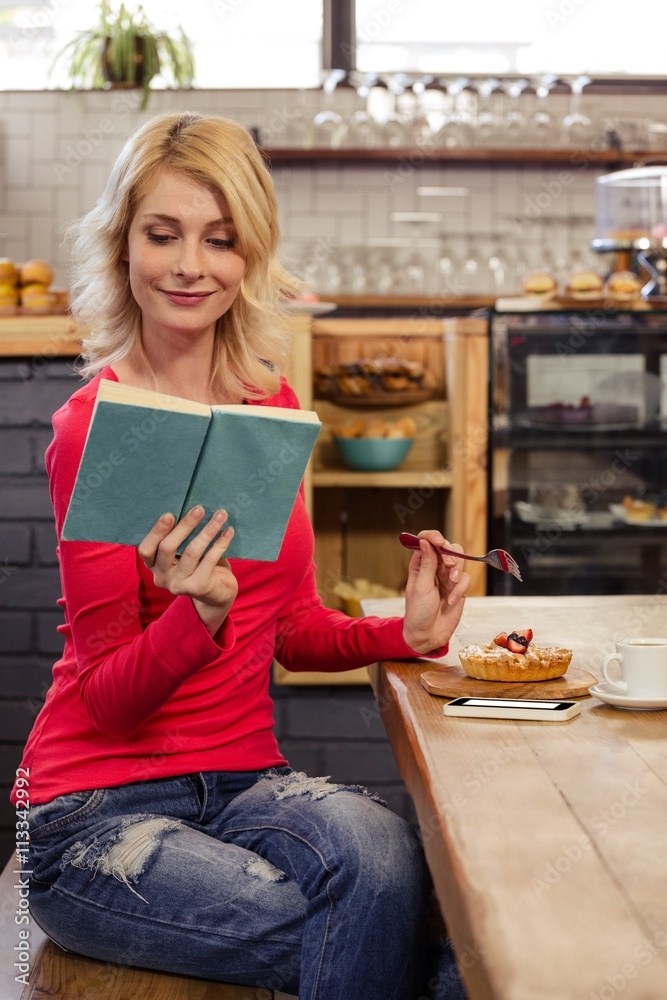 Woman reading a book and eating a cake