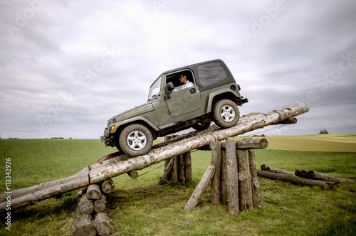 Happy man parking jeep on wooden logs at field photo