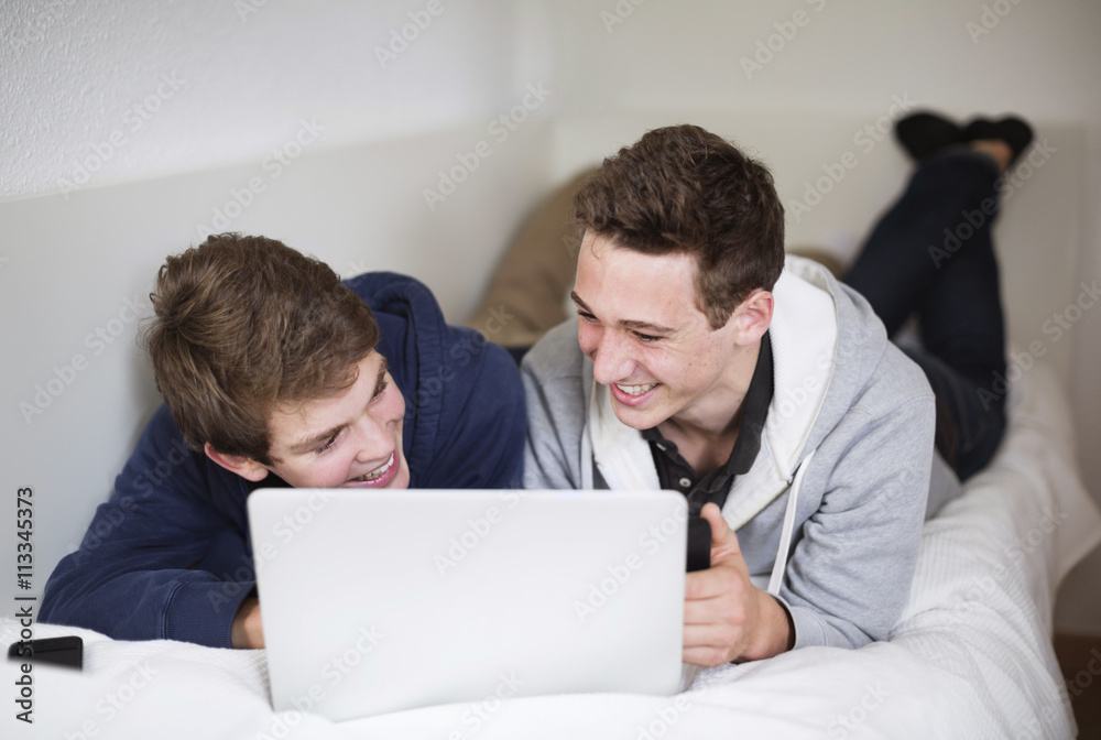Happy young boys using laptop together while lying in bed Happy young boys using laptop together while lying in bed