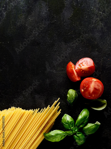 spaghetti, fresh basil and tomatoes on a dark rustic background