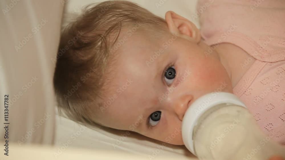 Beautiful, cute baby, lying in bed and drinking from a bottle for feeding.Little and cute baby, drinks from bottle with nipple. Beautiful, cute baby, lying in bed and drinking from a bottle for feeding.Little and cute baby, drinks from bottle with nipple.