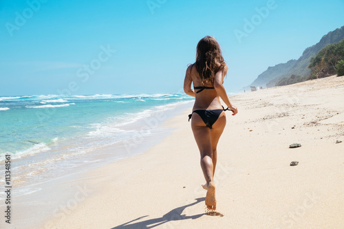 Woman running through sea water on a beach in Bali. Female runner jogging during outdoor workout on beach.