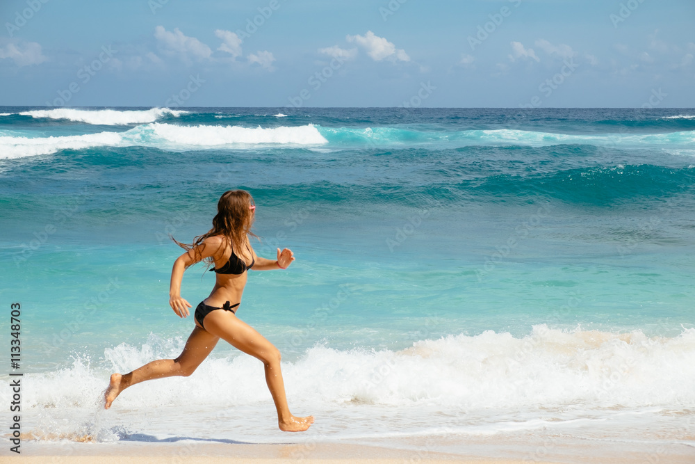 Woman running through sea water on a beach in Bali. Female runner jogging during outdoor workout on beach. Woman running through sea water on a beach in Bali. Female runner jogging during outdoor workout on beach.