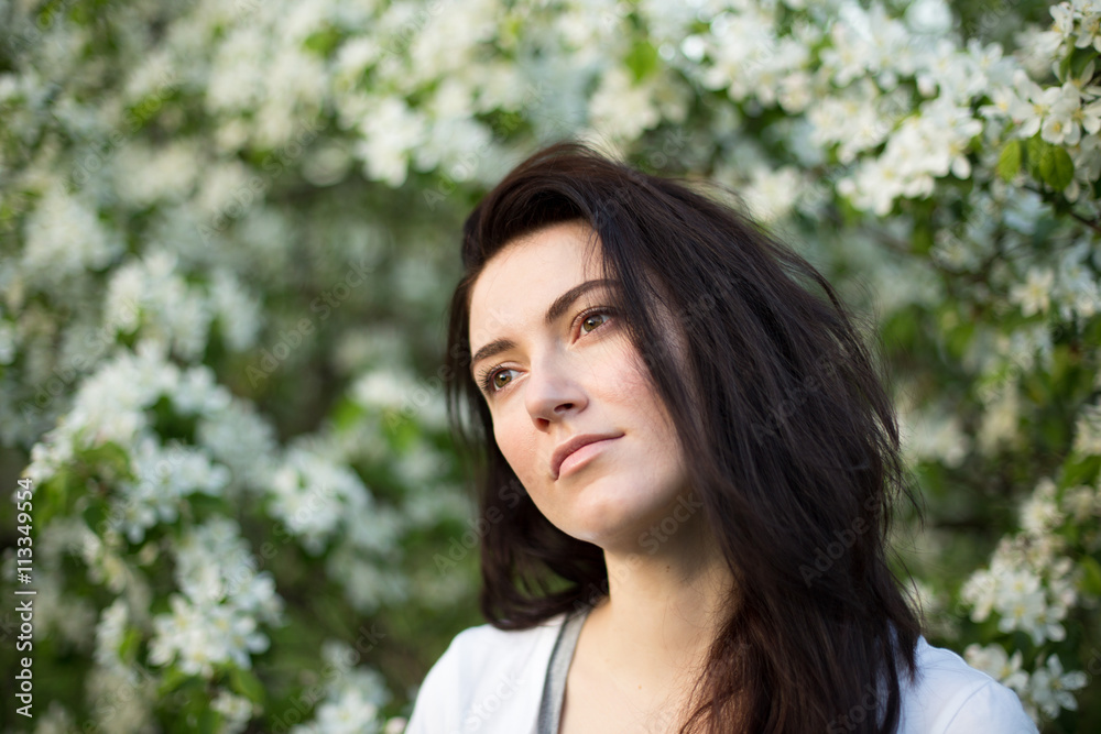 Young beautiful brunette woman in blooming apple tree garden