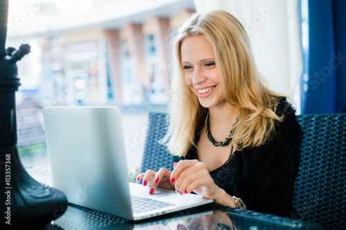 Smiling woman working with laptop outdoor at cafe